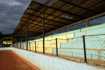 Metal fence by wall against sky