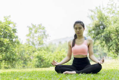 Full length of woman meditating while sitting on grassy field at park