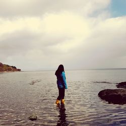 Rear view of woman standing on beach against sky