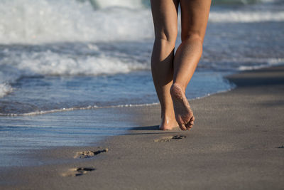 Low section of woman walking on shore at beach