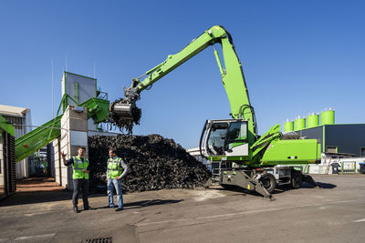 Man standing and discussing in front of excavator at recycling center