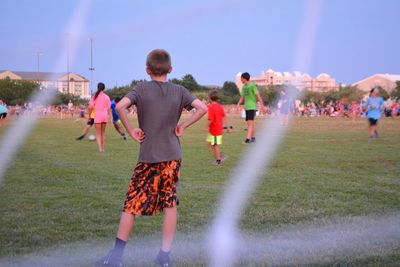 Rear view of boy standing on playing field seen through net