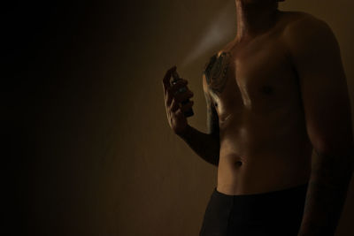 Shirtless man spraying perfume against black background