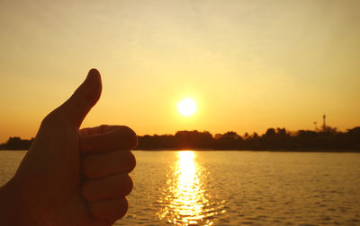 Cropped hand of woman holding sun at sunset