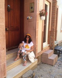 Full length portrait of smiling woman sitting on door