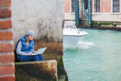 Woman using laptop while sitting on steps by canal
