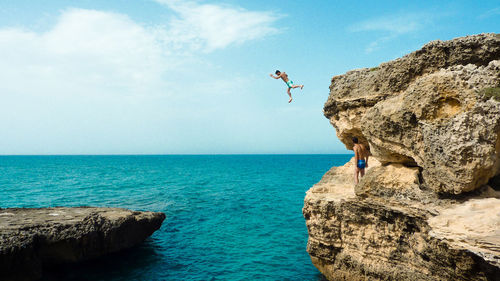 Man jumping from cliff in sea against sky