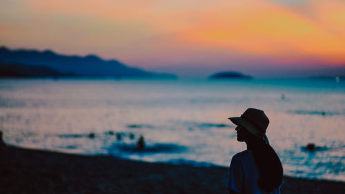 Rear view of silhouette woman standing at beach during sunset