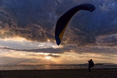 Silhouette person by sea against sky during sunset