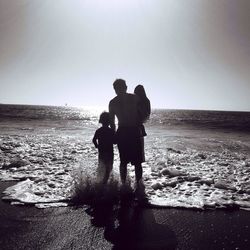 Silhouette friends standing on beach against clear sky