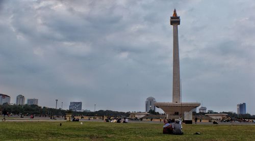 Group of people in front of buildings against cloudy sky