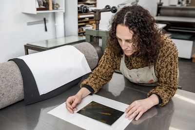 Female artist operating a manual vintage industrial printer.