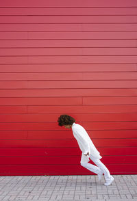 Young woman leaning forward on footpath by red wall