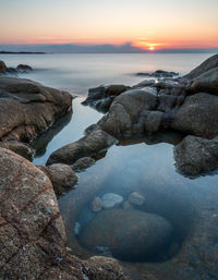 Rocks on beach against sky during sunset