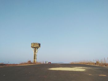 Water tower by road against clear sky