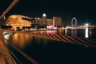 Illuminated bridge over river against buildings at night
