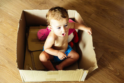 High angle portrait of cute boy sitting in box at home