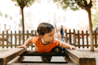 Boy looking away while sitting on wood