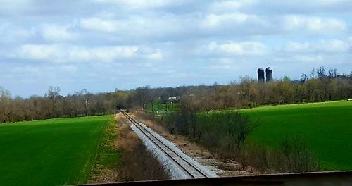 Road passing through field against cloudy sky