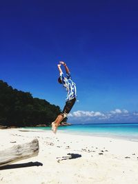 Man jumping at beach against blue sky