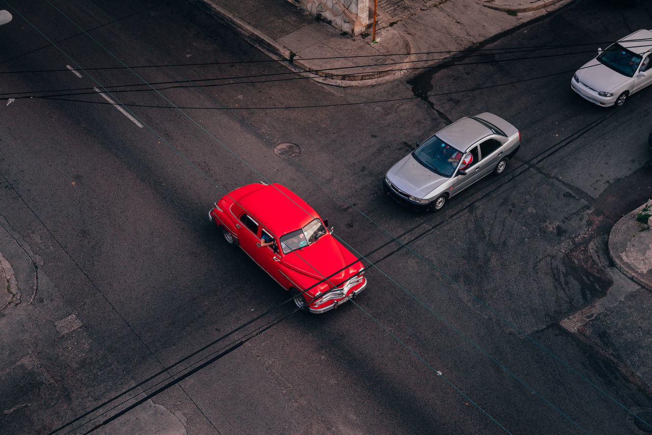From above of asphalt road intersection with red vintage car among contemporary transports in middle in cuba