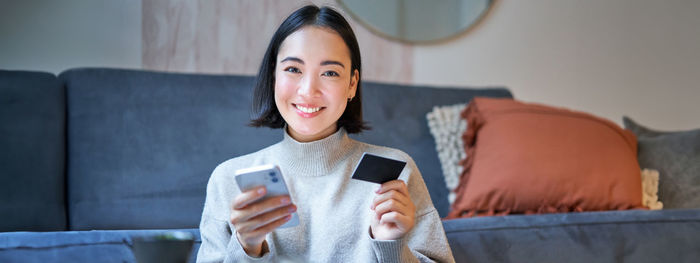 Portrait of young woman using mobile phone while sitting on sofa at home