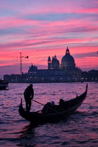 Silhouette man on boat in canal against sky during sunset