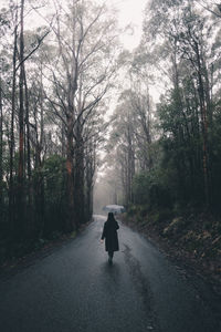 Rear view of woman walking on road in forest