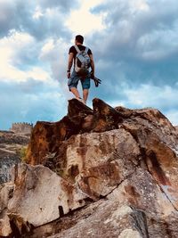 Low angle view of backpacker standing on rock formation against cloudy sky