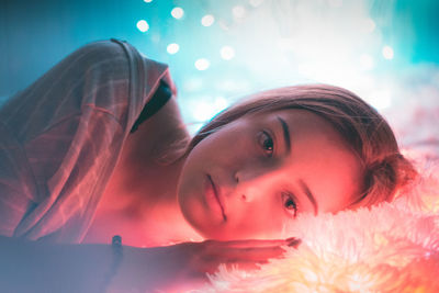 Close-up portrait of young woman lying down in illuminated room