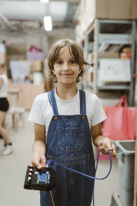 Portrait of smiling female student holding electrical part at workshop in school