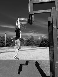 Boy hanging on basketball hoop against sky