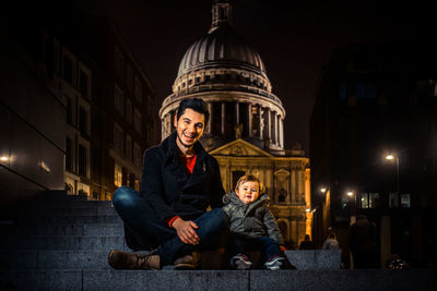 Portrait of happy friends sitting on illuminated city at night