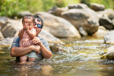 Father with daughter by rocks in river