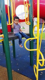 Full length of cute boy sitting on slide at playground