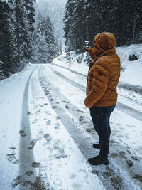 Man photographing while standing on snow covered road in forest during winter