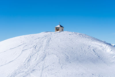 Low angle view of snow covered mountain and small chapel on top against clear blue sky