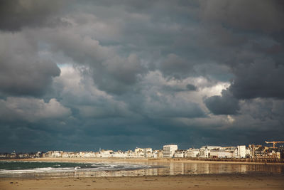 View of cityscape by sea against storm clouds