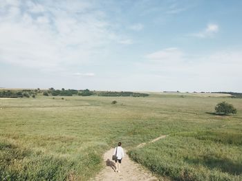 Rear view of man walking on field against sky