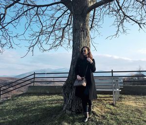 Young woman standing by bare tree on mountain against sky