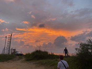 Rear view of people standing on street against sky during sunset