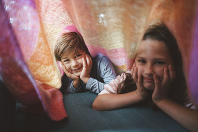 Happy brother and sister lying with head in hands under blanket