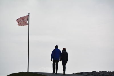 Rear view of couple walking by flag against sky