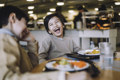 Boy laughing while sitting with friend during lunch break at school