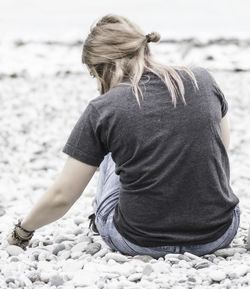 Rear view of woman sitting on pebbles at beach