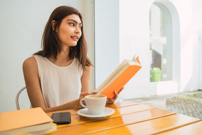 Smiling businesswoman holding book looking away while sitting at cafe