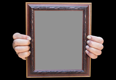 Cropped hands of person holding blank picture frame against black background