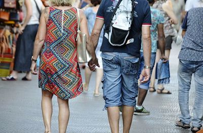 Midsection of couple holding hands while walking on street