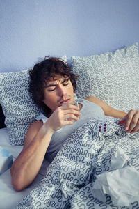 Young man drinking water on bed at home