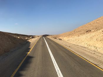 Road leading towards mountain against clear sky